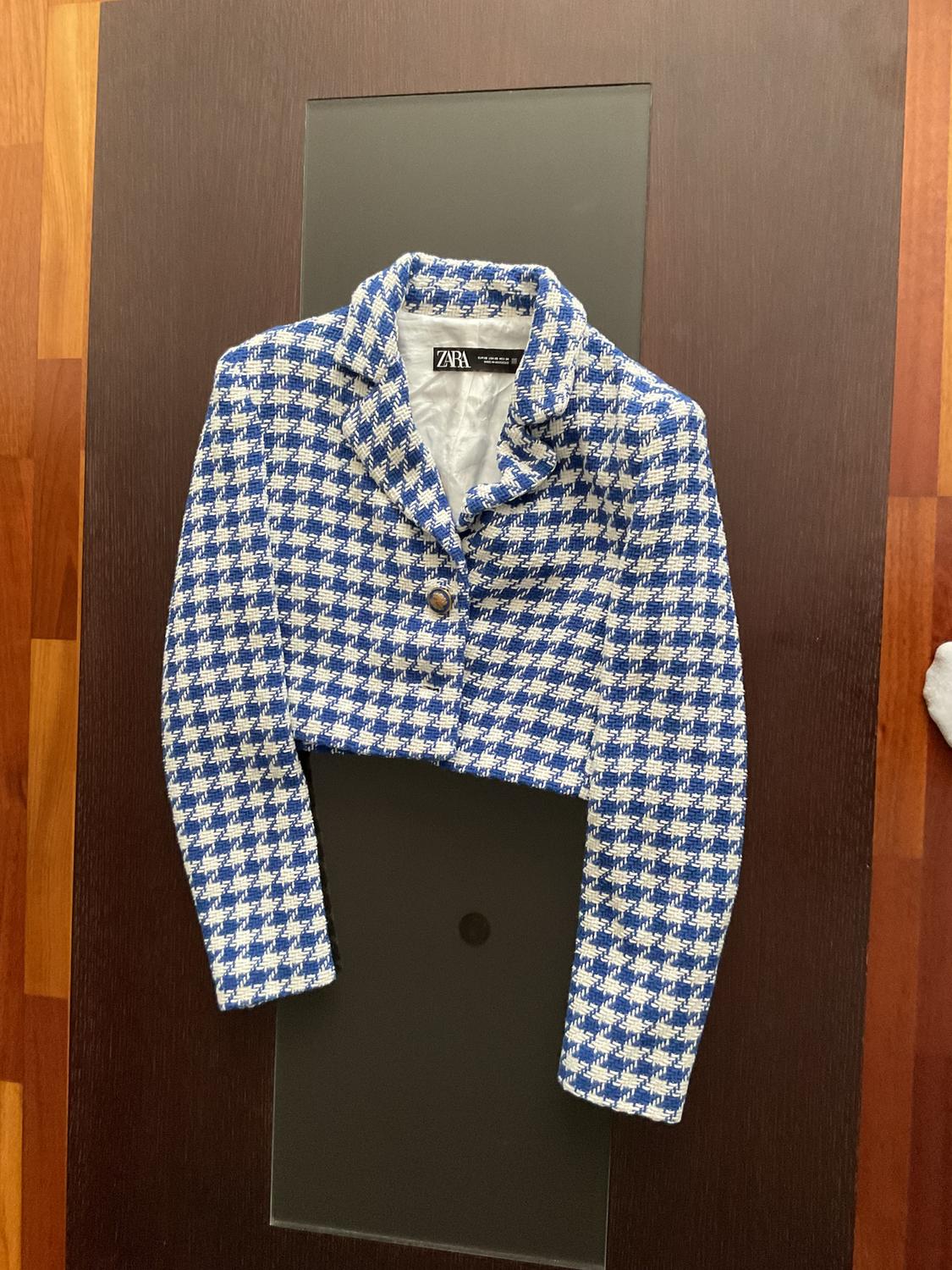 Blue and white checked short jacket on a dark table. Visible label with the text "ZARA".