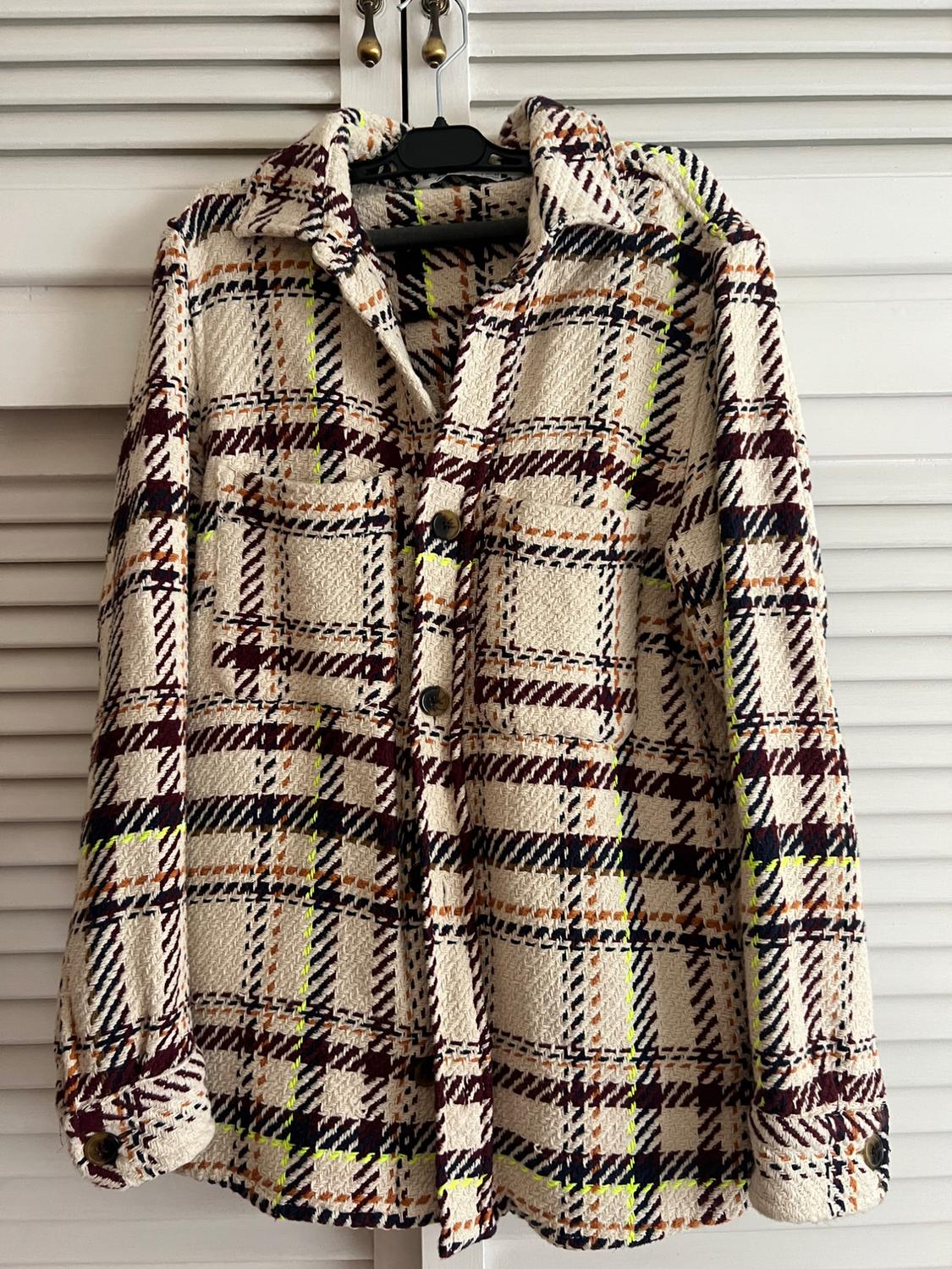 Checkered jacket in shades of cream, brown and neon yellow, hanging on a hanger in front of white doors.