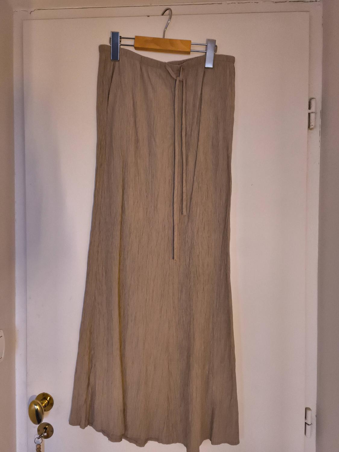 Long beige skirt hanging on a wooden hanger over a white door. The skirt has a tie at the waist.
