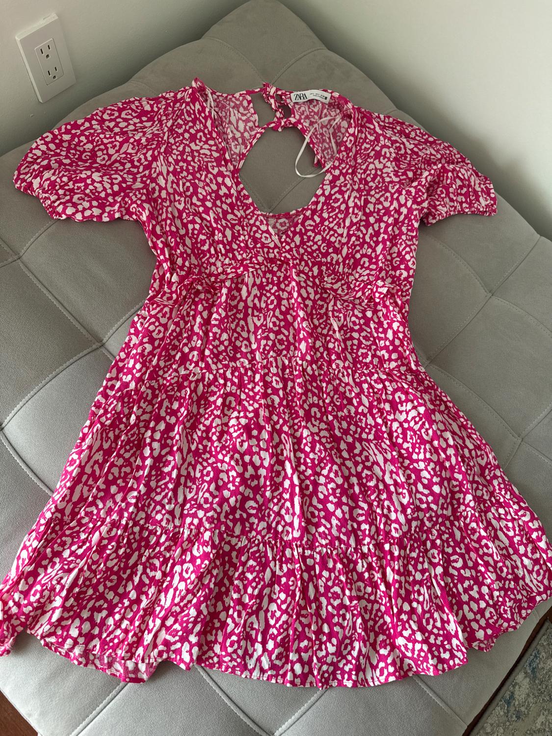 Pink dress with white pattern, short sleeves, and a backless design, on a grey sofa. Visible label on the collar.