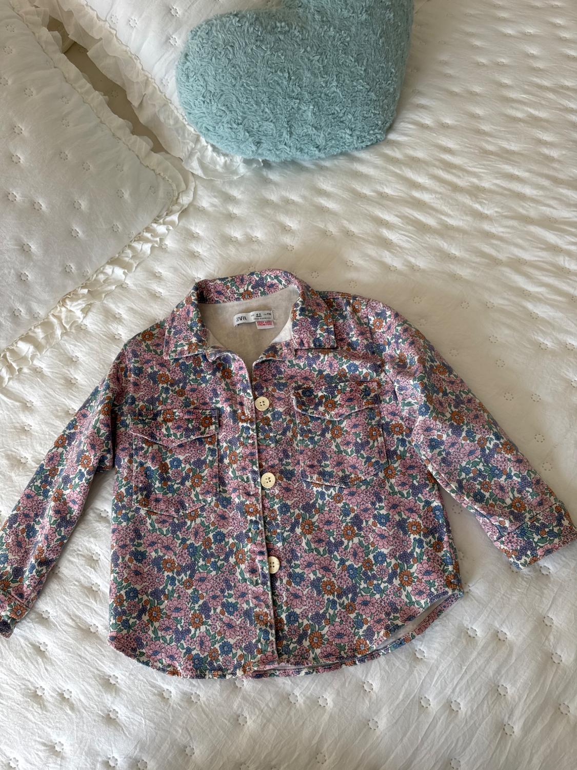 Long-sleeved shirt with a floral print in pink and blue tones on a white bed with a blue heart-shaped cushion.