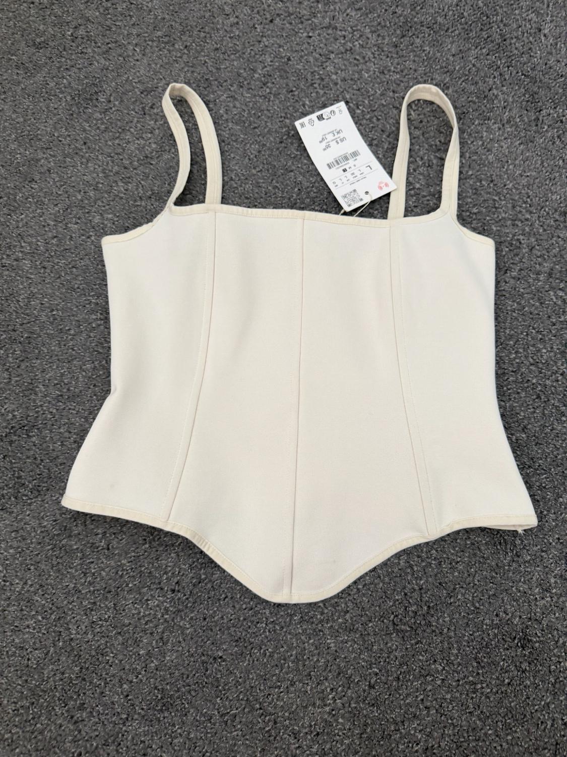 White vest top with vertical seams and a V-shaped hem, placed on a textured grey surface.