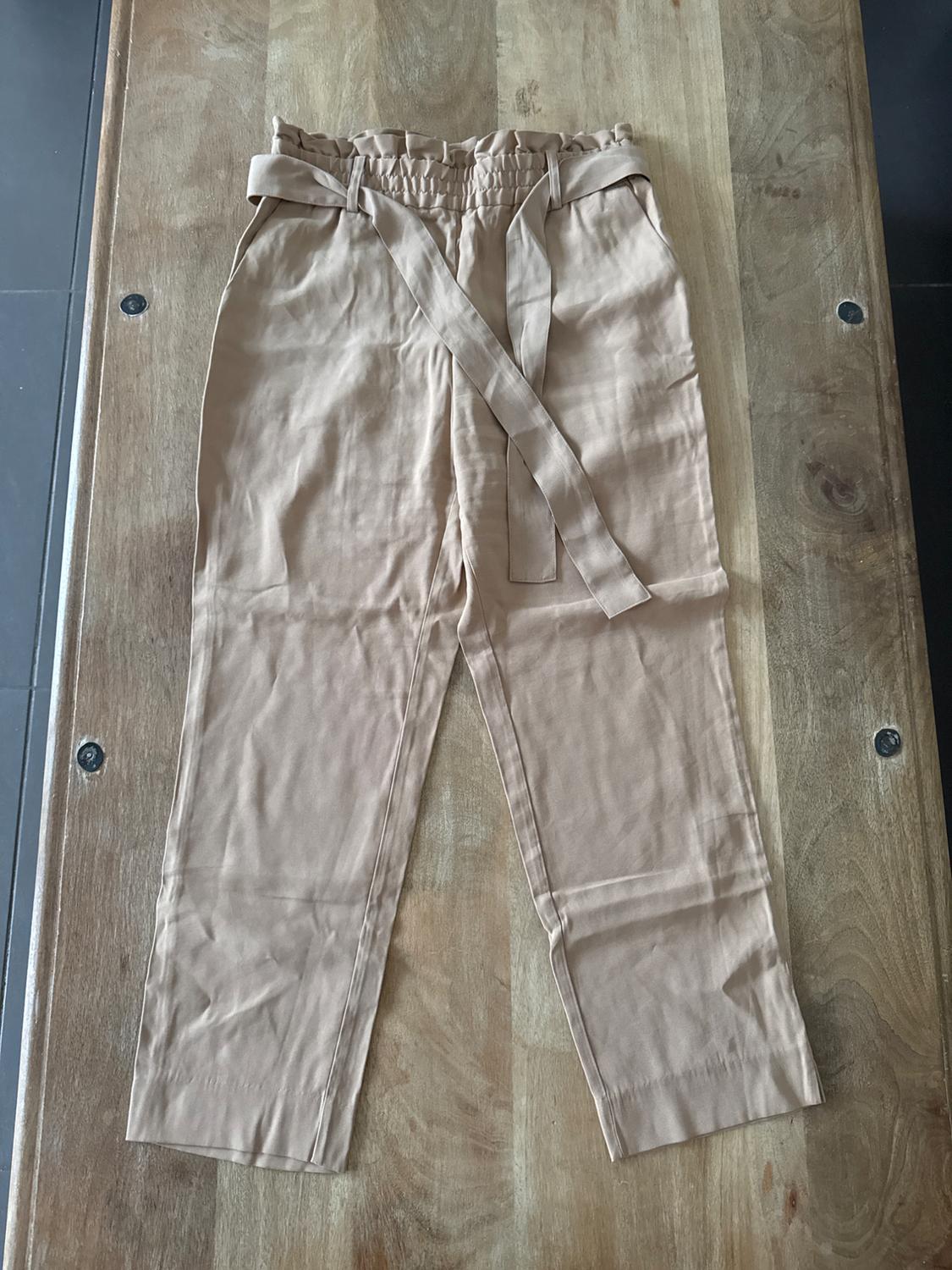 Beige lightweight trousers with matching belt, laid out on a wooden table.