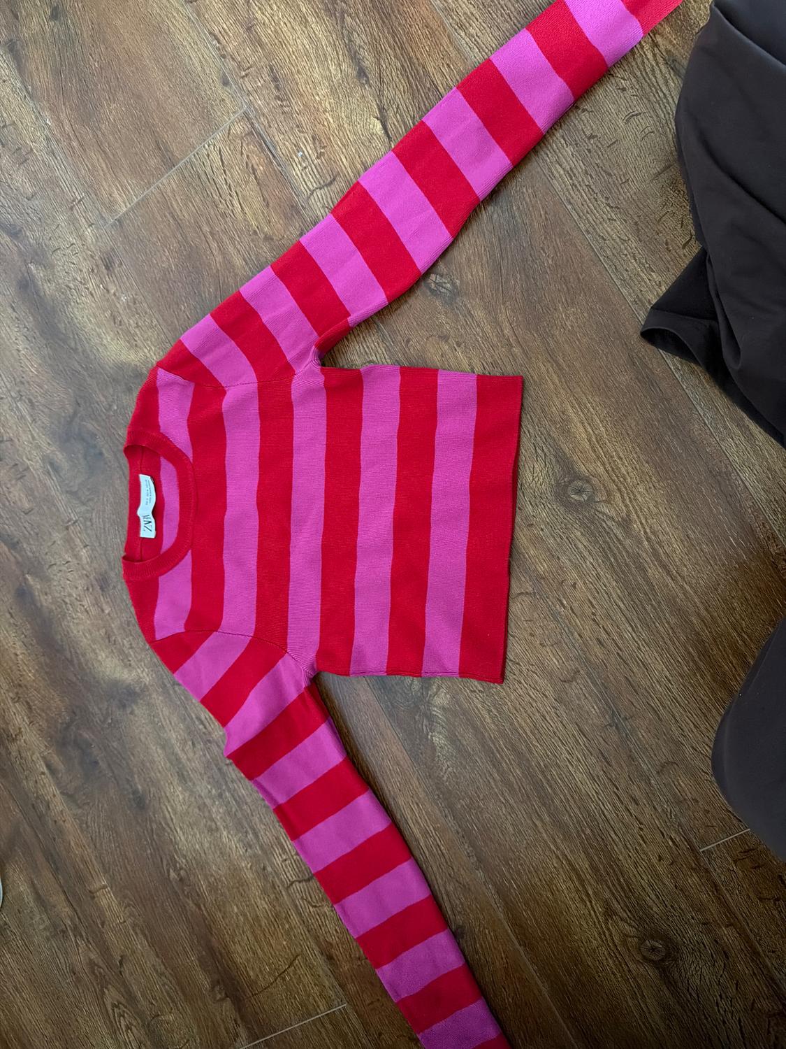 Red and pink horizontal striped jumper on a wooden floor. Long sleeves and a round neck.