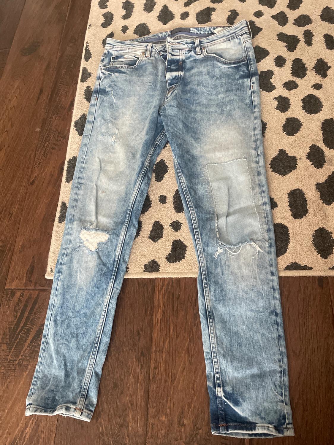 Light blue distressed jeans with ripped knees, on a black-spotted rug and hardwood floor.