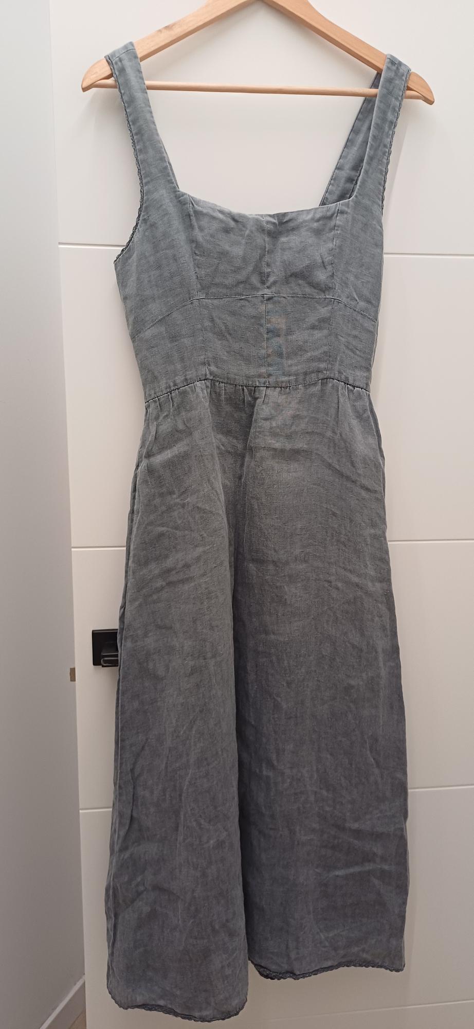 Grey maxi dress with wide straps hanging on a wooden hanger against a white door with a black handle. Minimalist style.