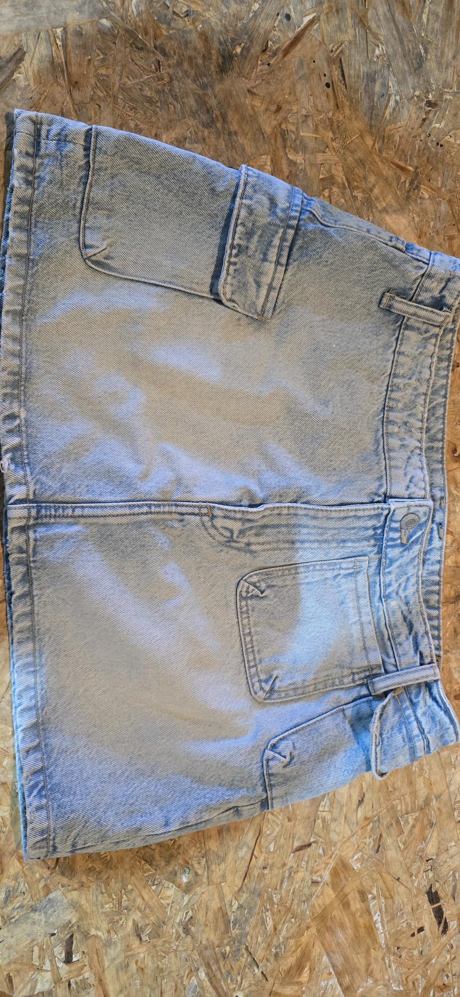 Light blue denim skirt with large pockets, placed on a wooden surface with visible texture.