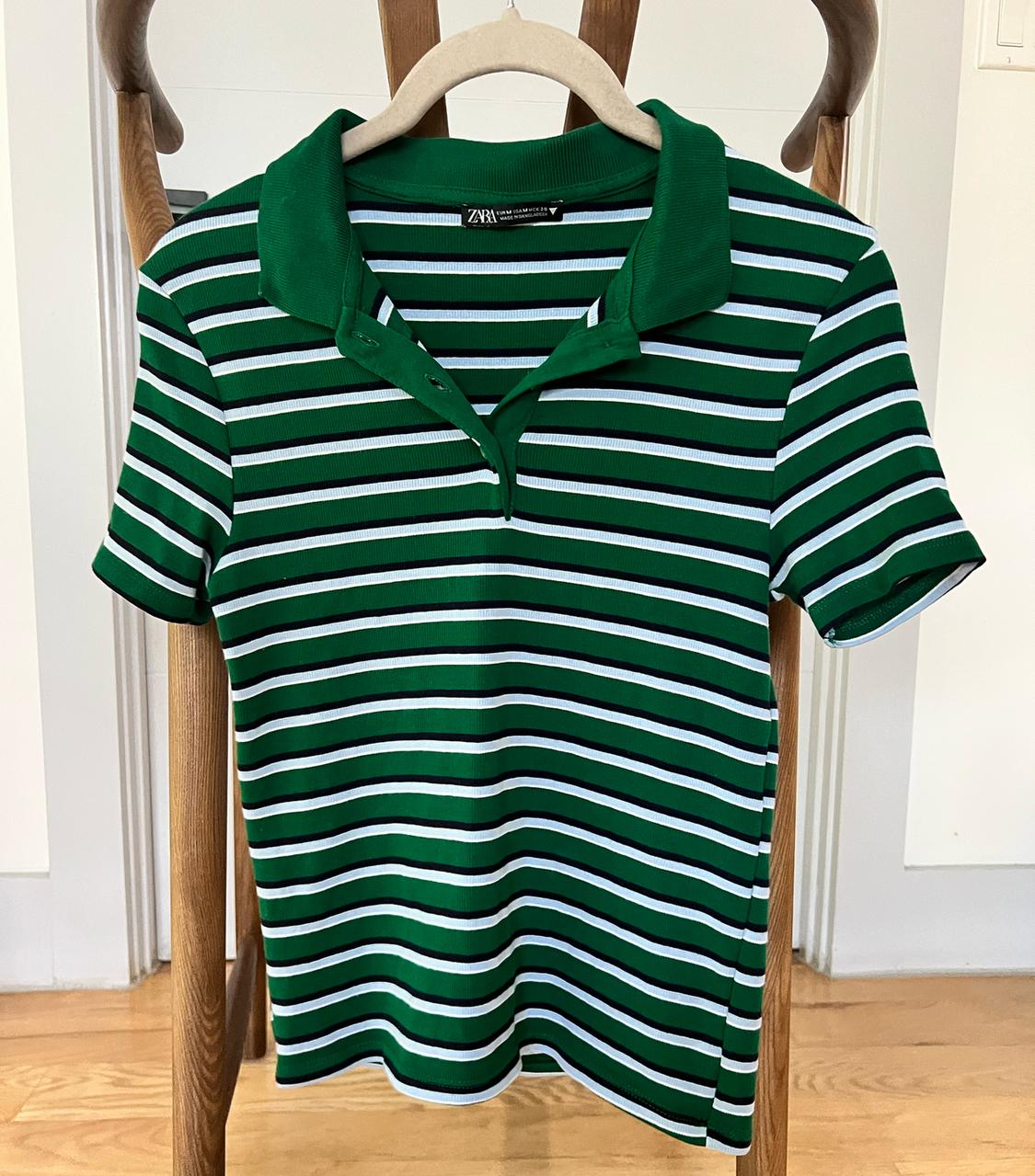 Green and white striped polo shirt hanging on a wooden chair. Interior background with light wood floor.