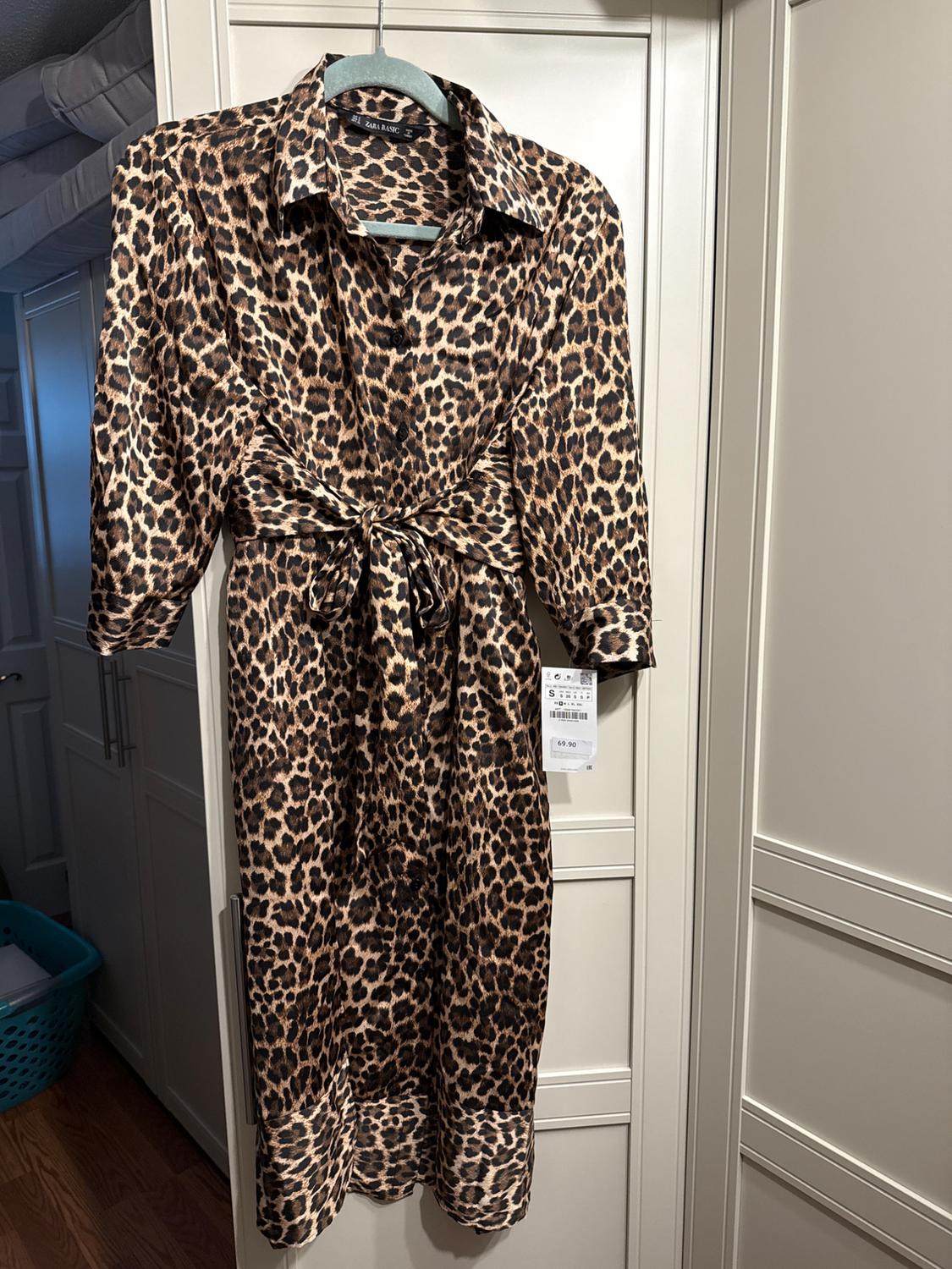 Animal print dress with waist tie, hanging on a hanger. Visible tag with price 69.90. White closet background.