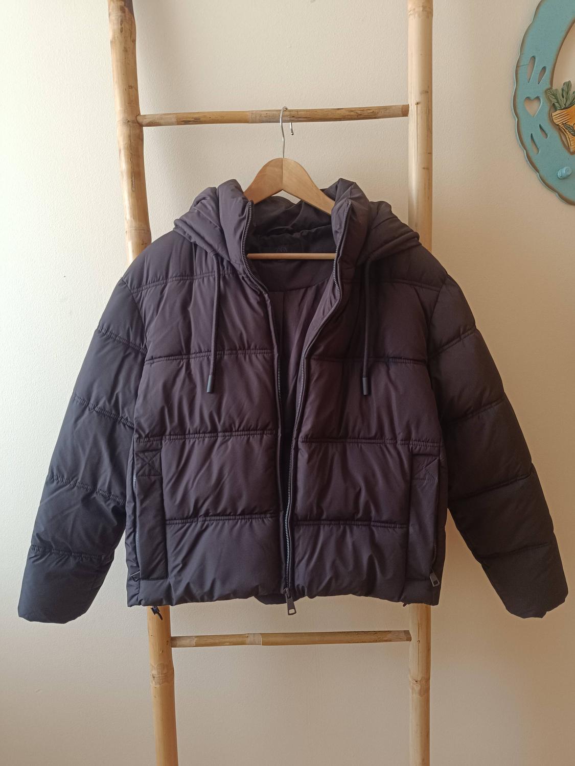 Black padded jacket with a hood hanging on a bamboo ladder. White background with a blue ornament on the wall.
