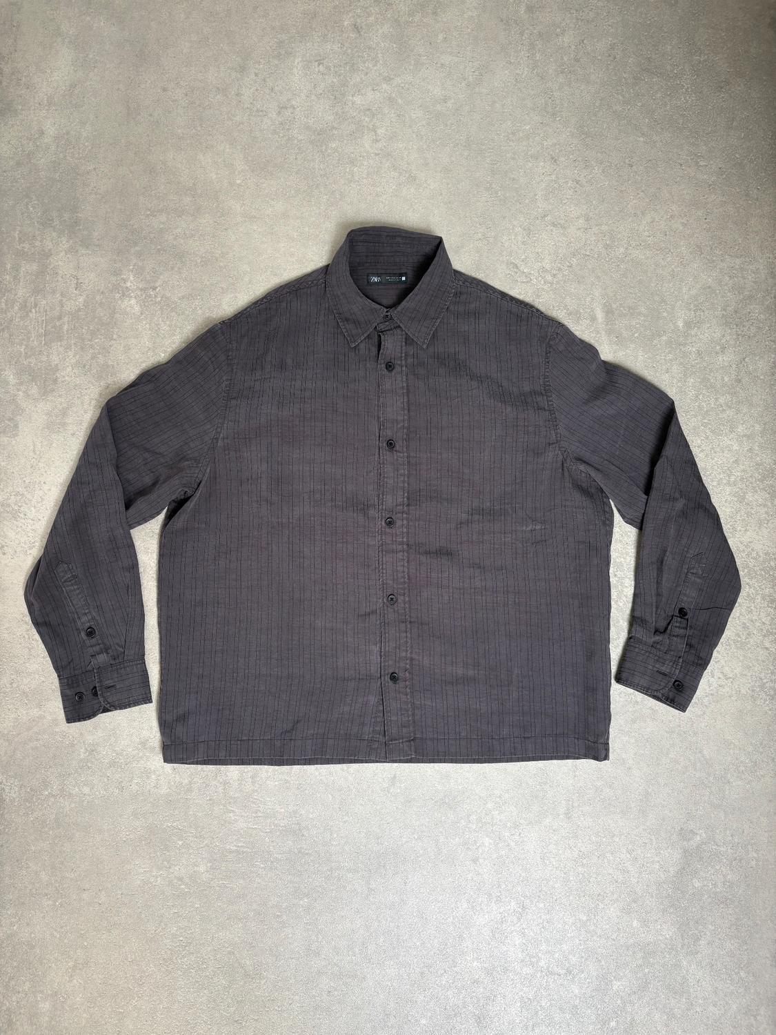 Grey long-sleeved shirt with black buttons, classic collar, and fine stripe texture, on a light grey background.