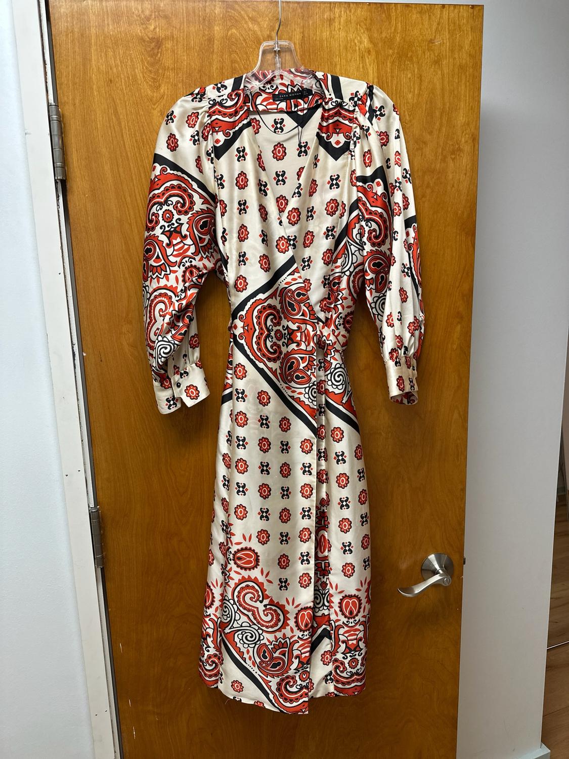 Long-sleeved wrap dress with a red and black print on a light background, hanging on a wooden door.