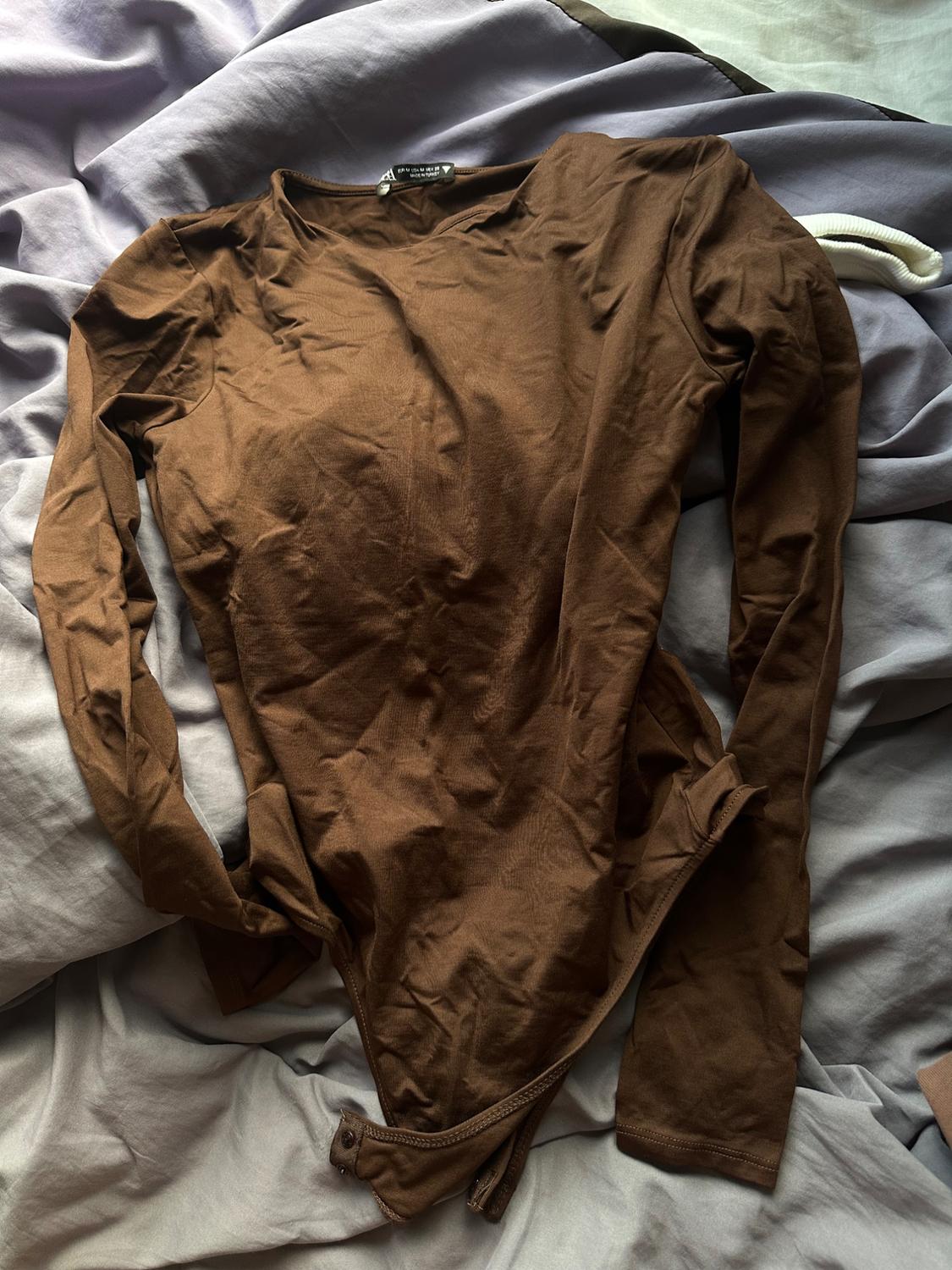 Wrinkled brown long-sleeved t-shirt on grey and white sheets. Label visible on the collar.