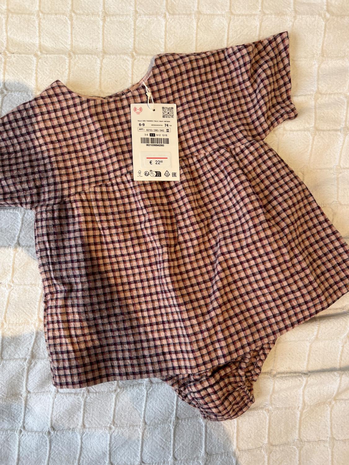 Baby's brown and pink checked romper suit on a white quilt. Visible label with price of £22 and size 6-9 months.