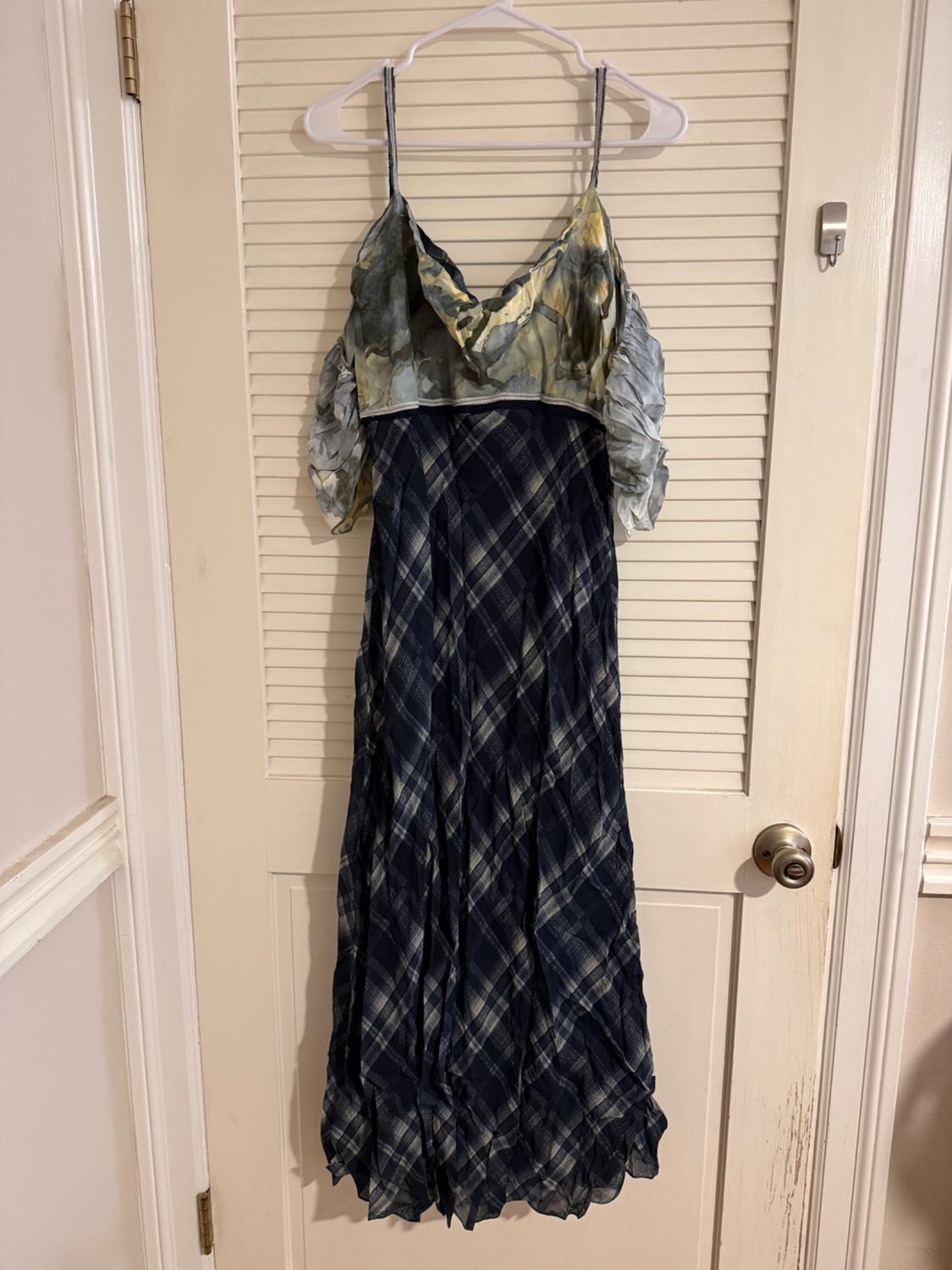 Long dress hanging on a door, with thin straps, a printed top in green and blue tones, and a blue checked skirt.