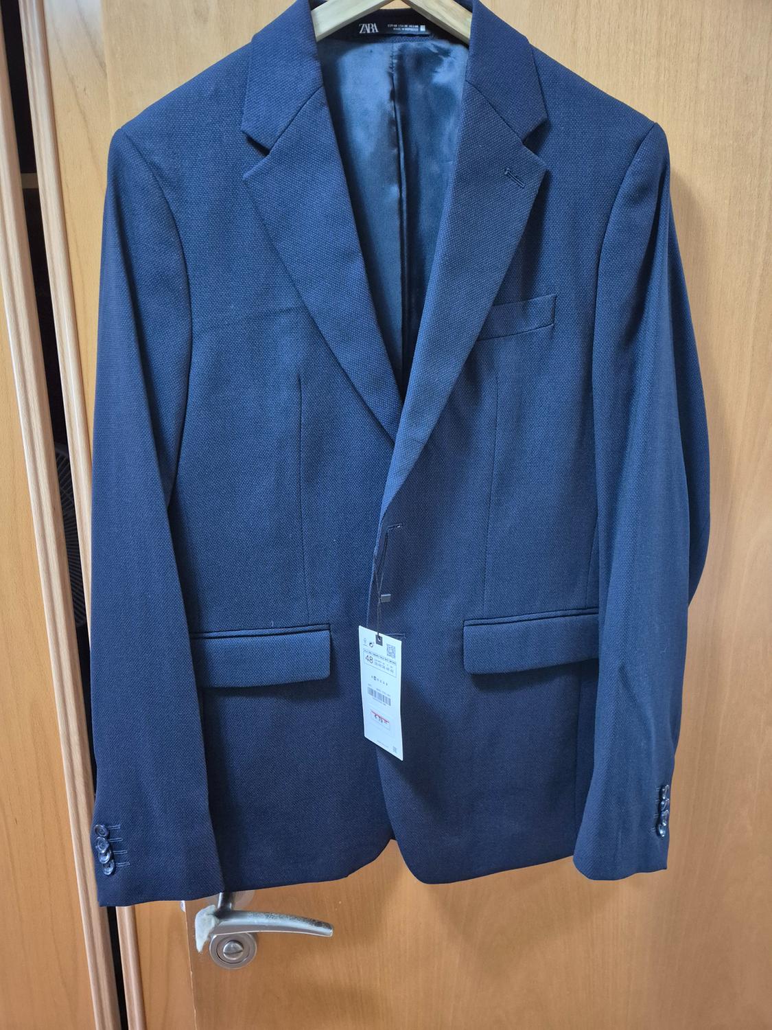 Blue jacket hanging on a wooden door, with a visible label on the left sleeve.