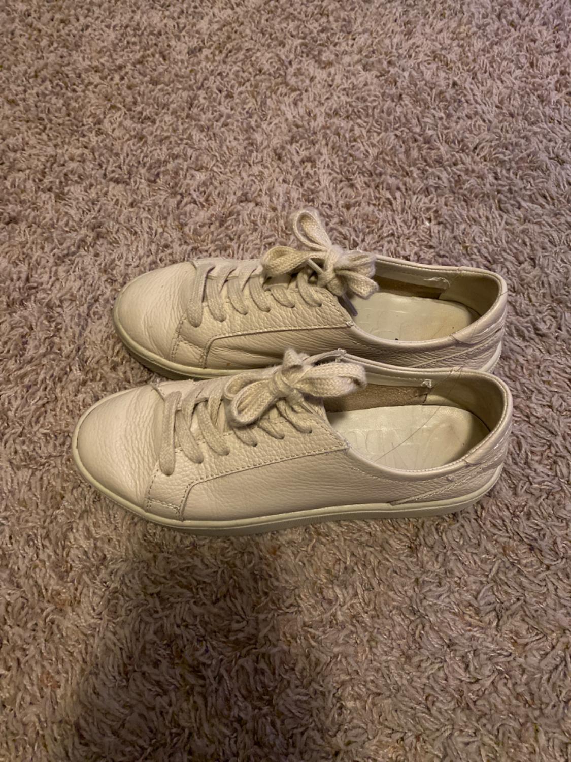 Beige leather lace-up trainers on a light brown rug. Casual and relaxed style.