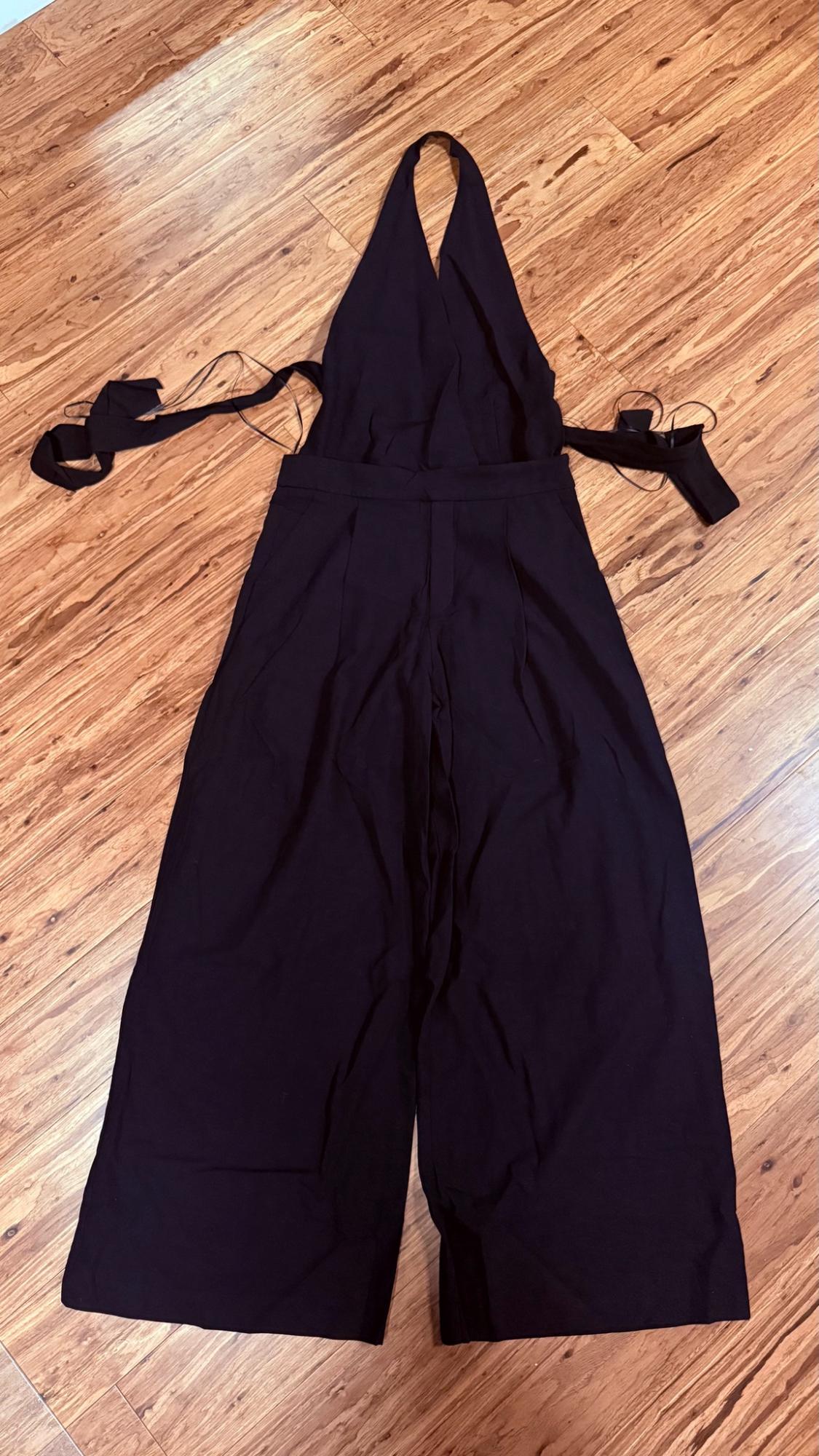Black halter-neck wide-leg jumpsuit with side straps, laid out on a wooden floor.