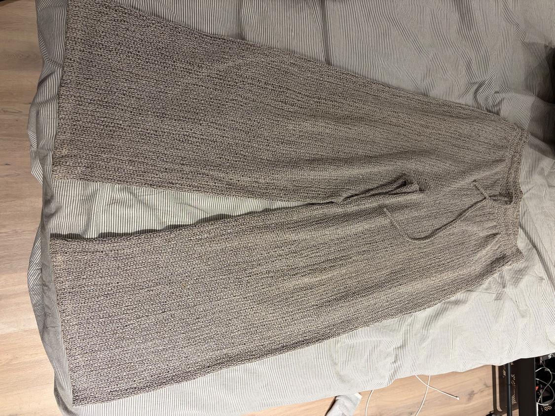 Grey knitted wide-leg trousers with a drawstring waist, placed on a striped fabric surface.