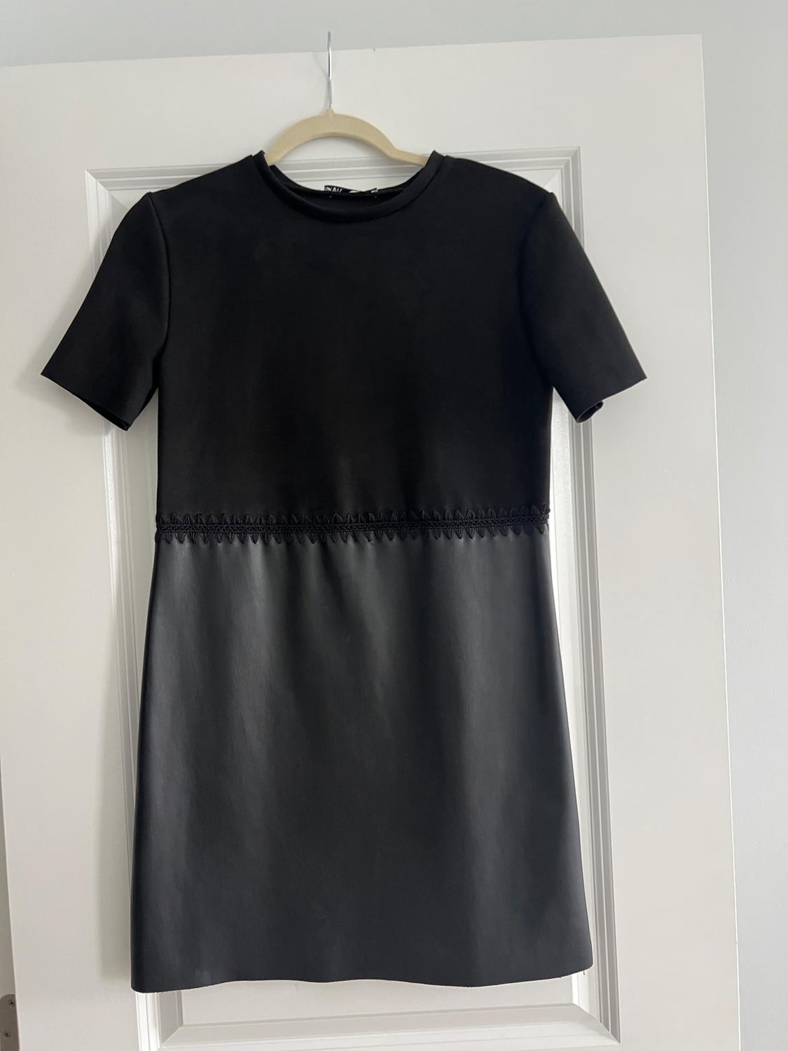 Short-sleeved black dress hanging on a white door. Decorative stitching detail at the waist.