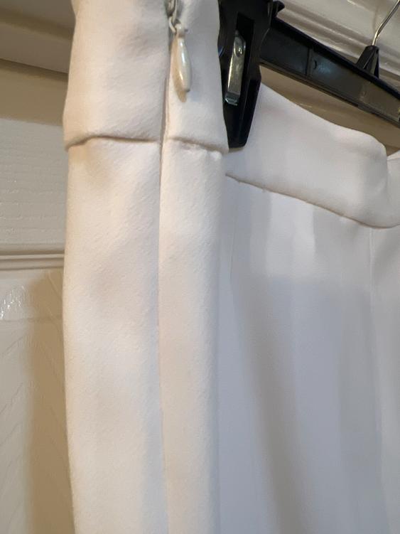 Detail of a white garment hanging on a black hanger. The fabric appears soft and is well-lit.