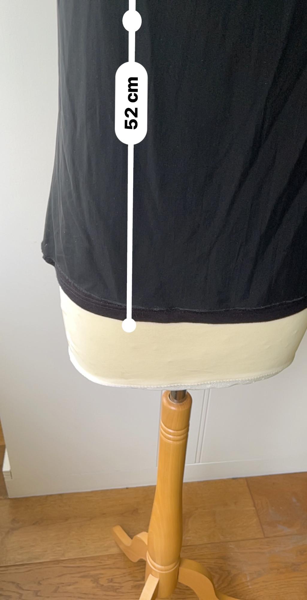 Lower section of a mannequin wearing a black T-shirt. Text in the image: "52 cm". Wooden base on a light wooden floor.