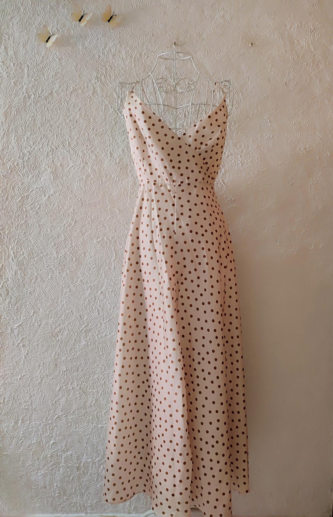 Long brown polka dot dress on a cream background on a wire mannequin, with decorative butterflies on the textured wall.