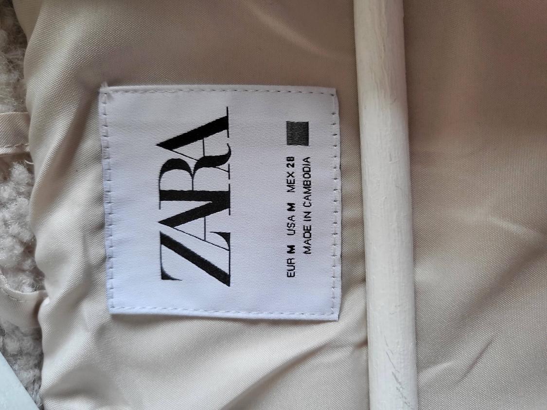 White clothing label with "ZARA", "EUR M USA M MEX 28", "MADE IN CAMBODIA" text on beige fabric.