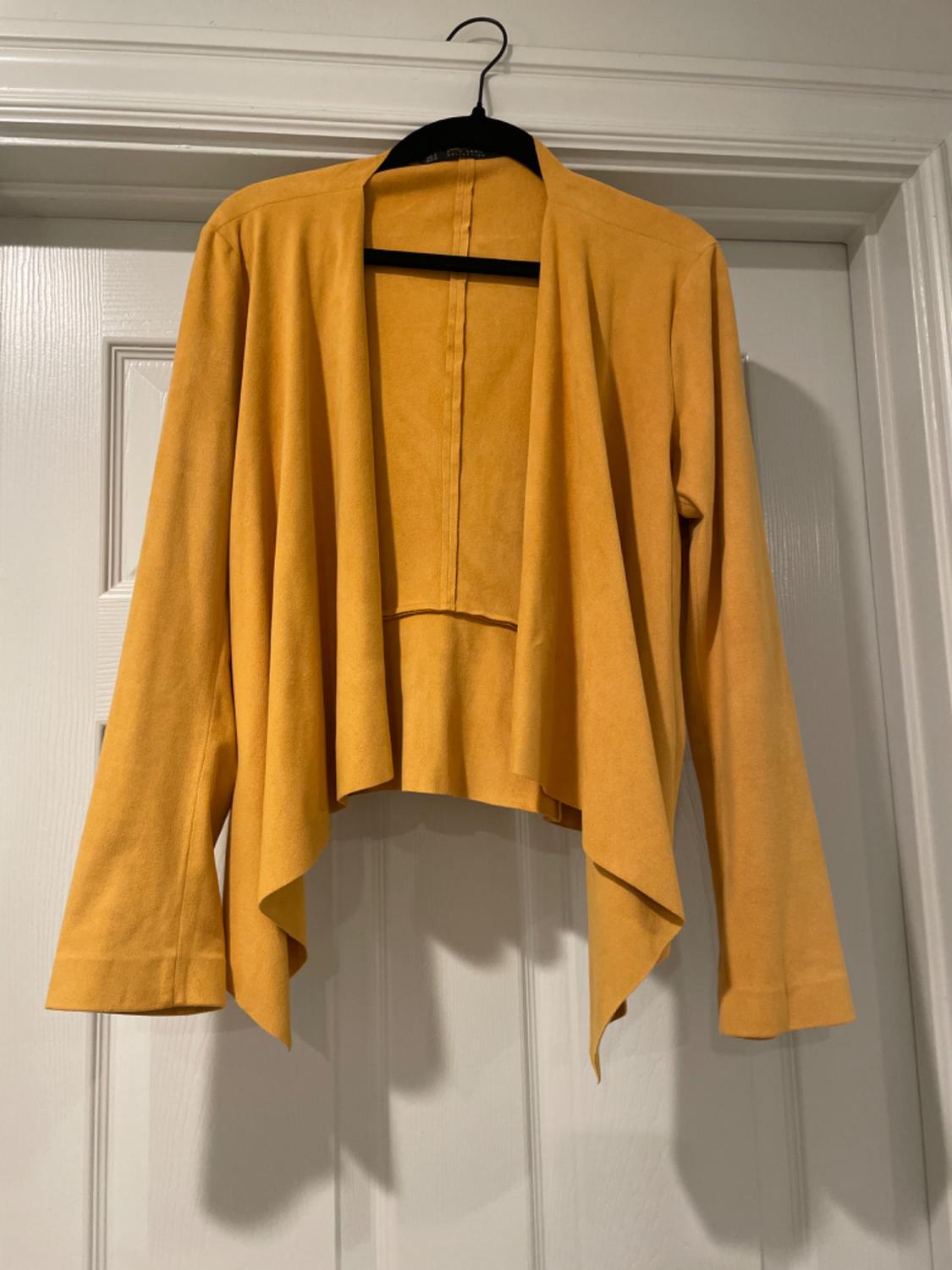 Front view of a yellow jacket with long sleeves and an asymmetric design, hanging on a hanger.