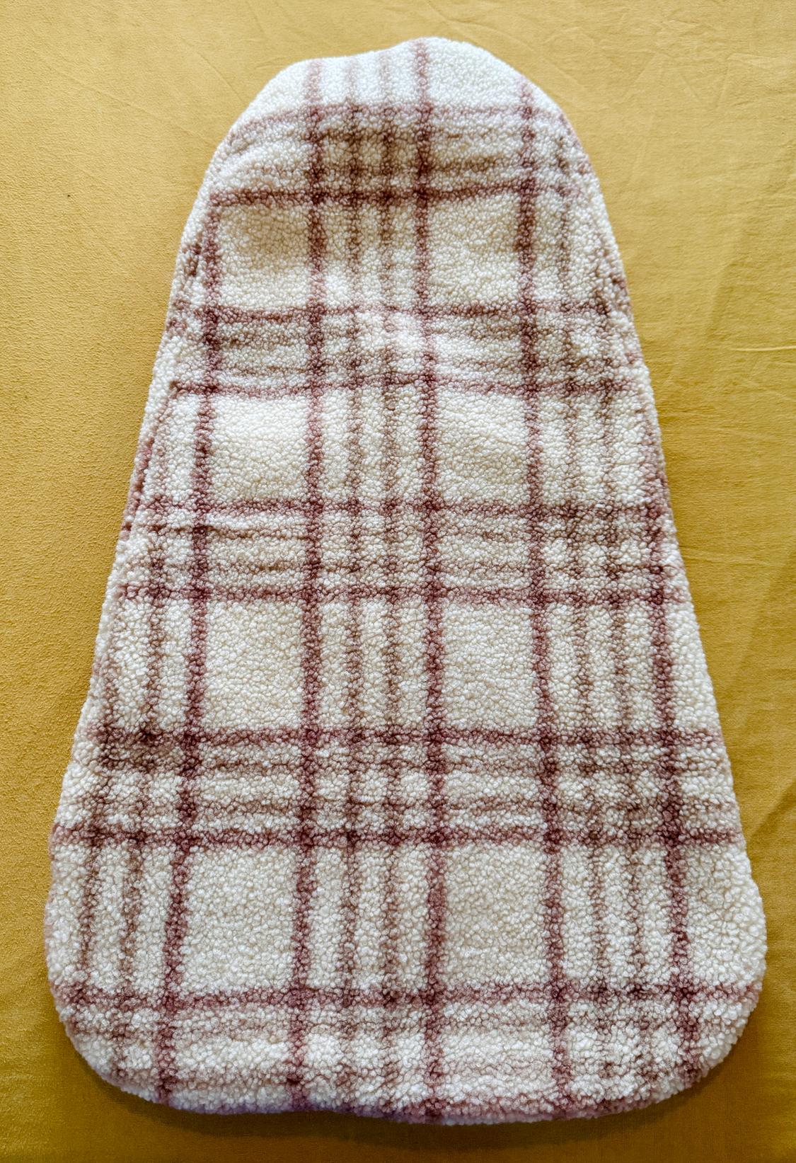 Soft fabric accessory with a brown check pattern on an ecru background, resting on mustard fabric. Relaxed and warm style.
