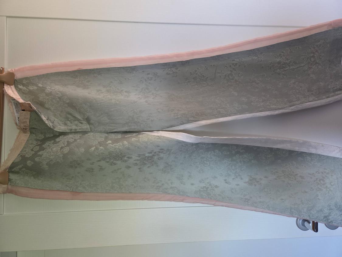 Grey fabric trousers with a floral print and pink trim, hanging on a wooden hanger against a white background.