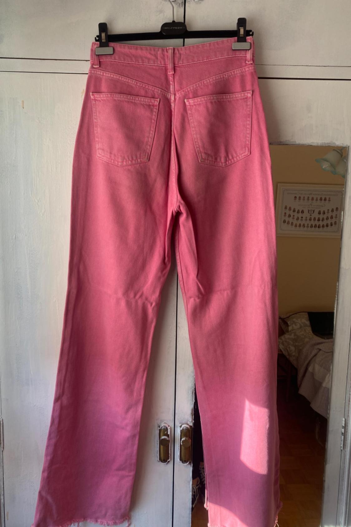 Rear view of pink trousers with back pockets and frayed hem.
