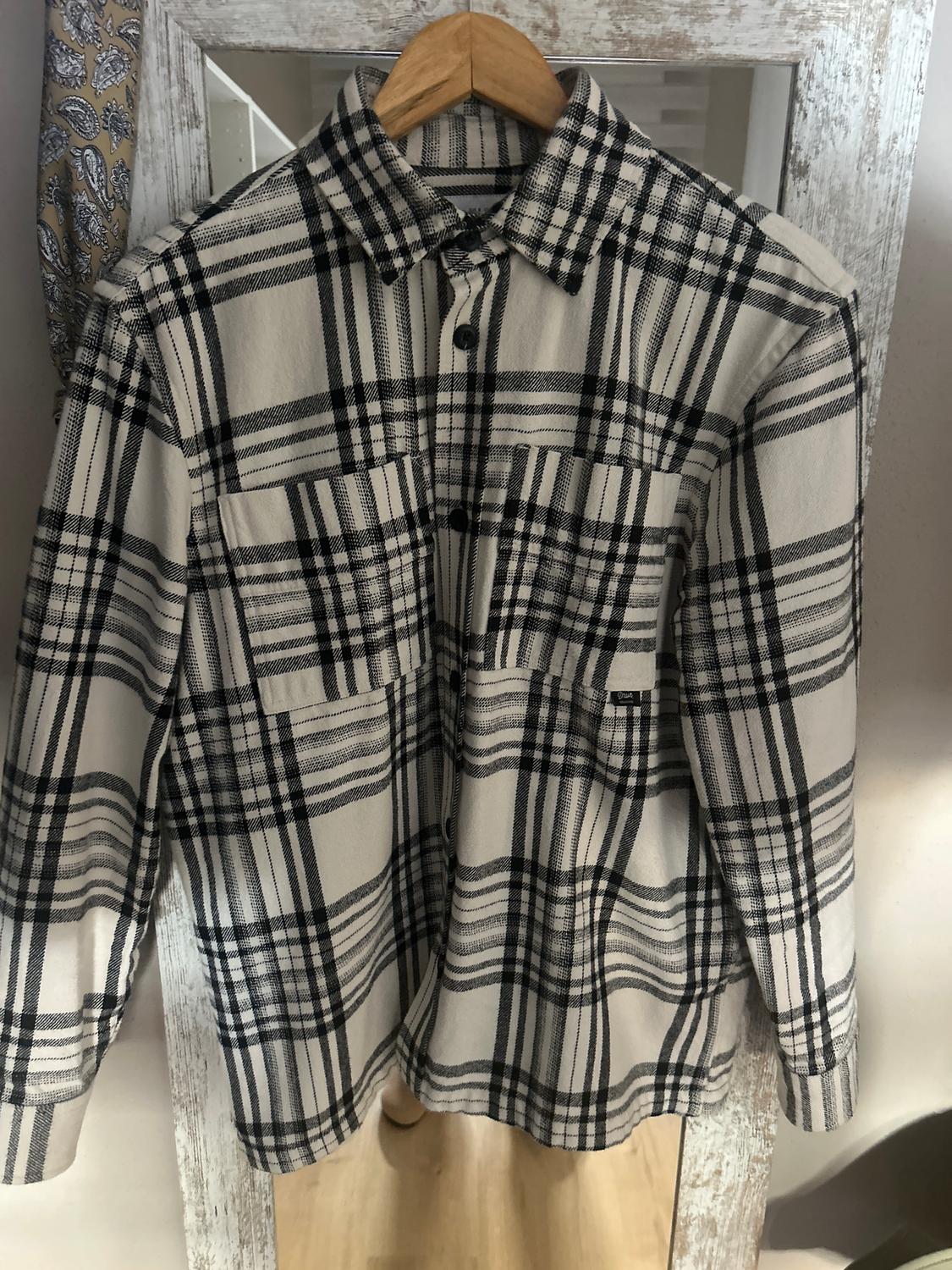 Black and white checked shirt hanging on a wooden hanger in front of a distressed white-framed mirror.