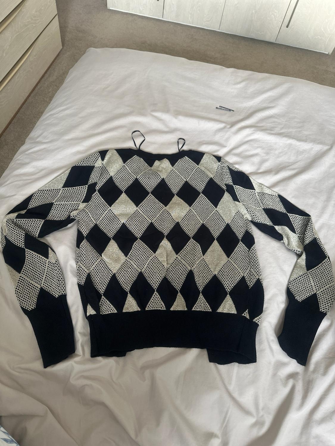Long-sleeved jumper with a black and silver argyle pattern, laid out on a white bed in a relaxed setting.