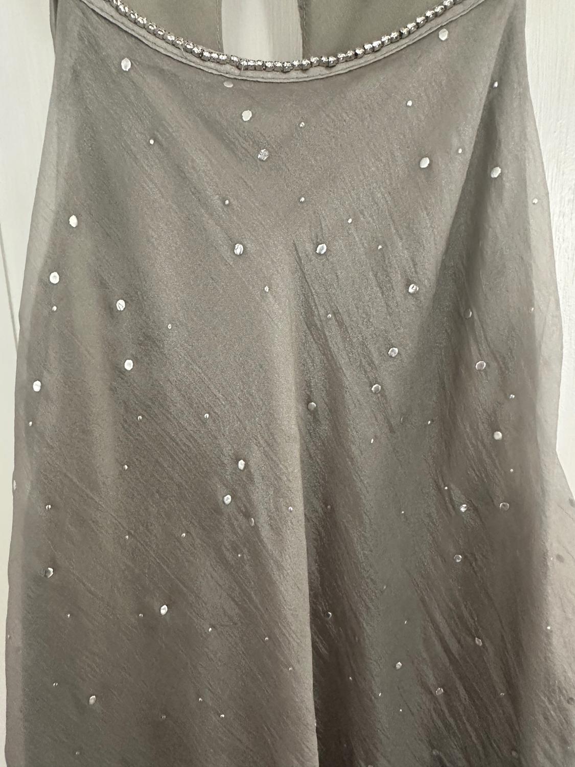 Detail of a gray semi-sheer knit garment with small scattered sparkles and a rhinestone trim along the neckline.