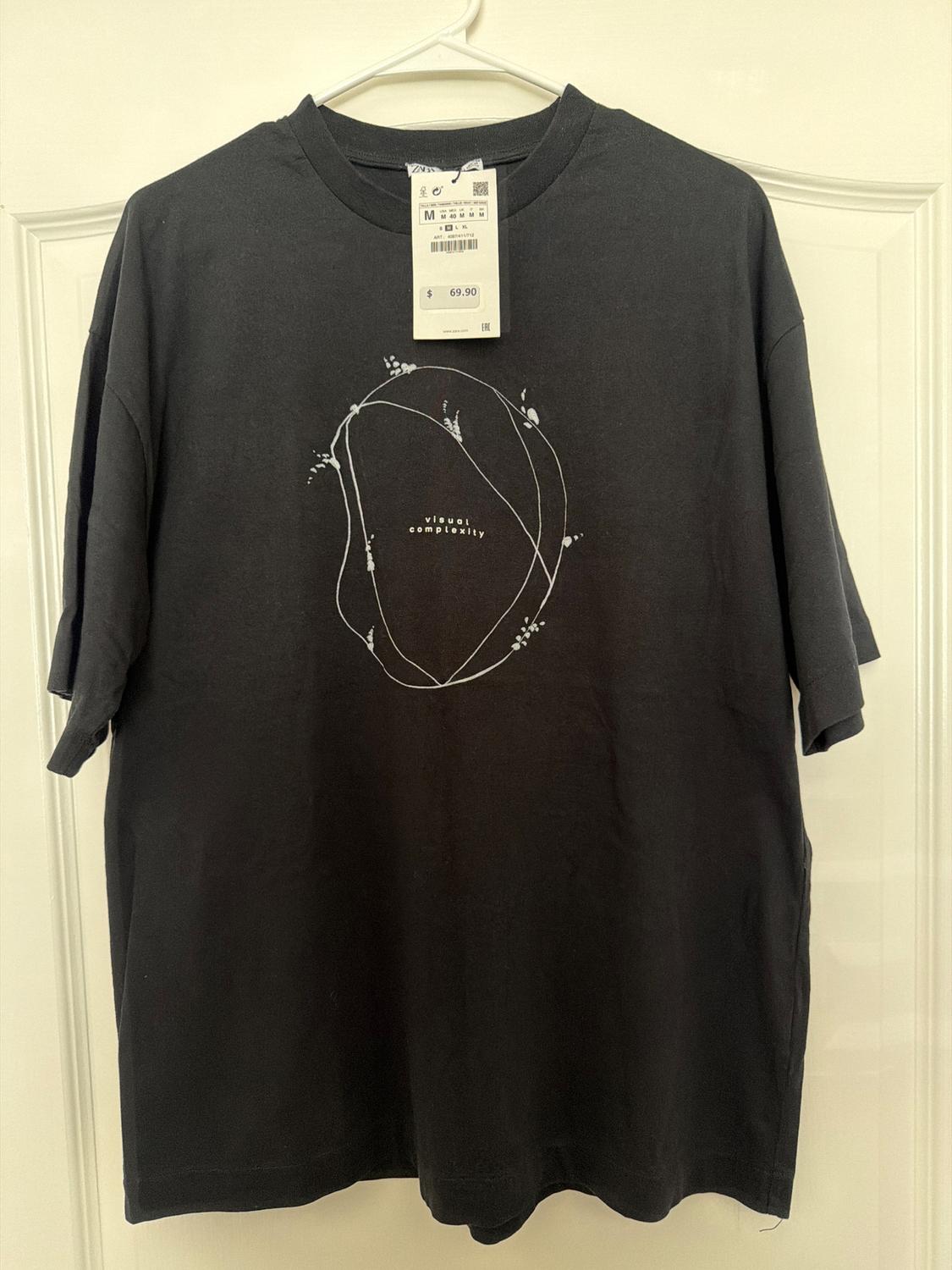 Black t-shirt hanging with a graphic design of lines and text "visual complexity". Visible price tag: $69.90, size M.