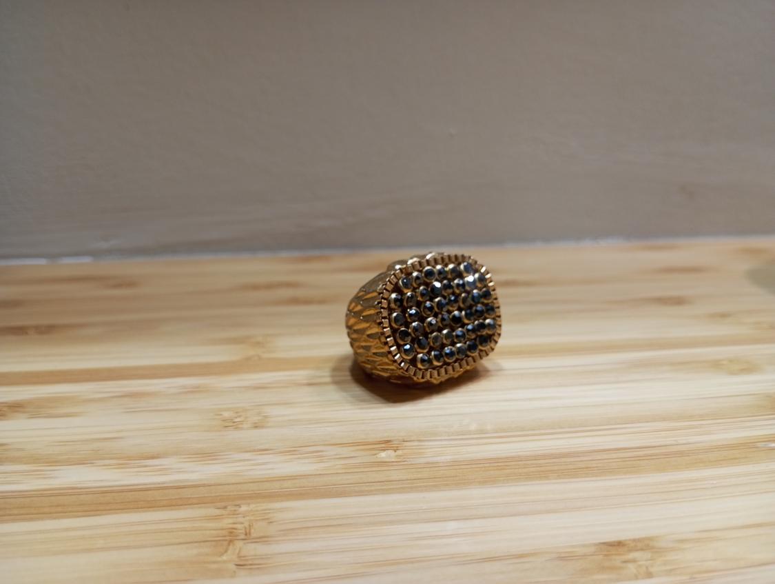 Gold ring with a sparkling beaded design on a light wooden surface. Neutral background and beige wall.