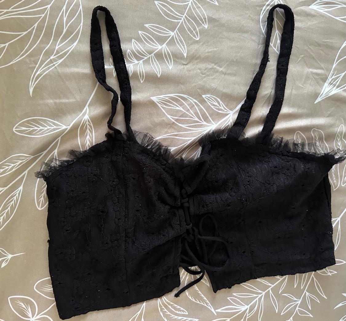 Black lace camisole with thin straps and a bow detail on the front, over a beige fabric with a white leaf print.