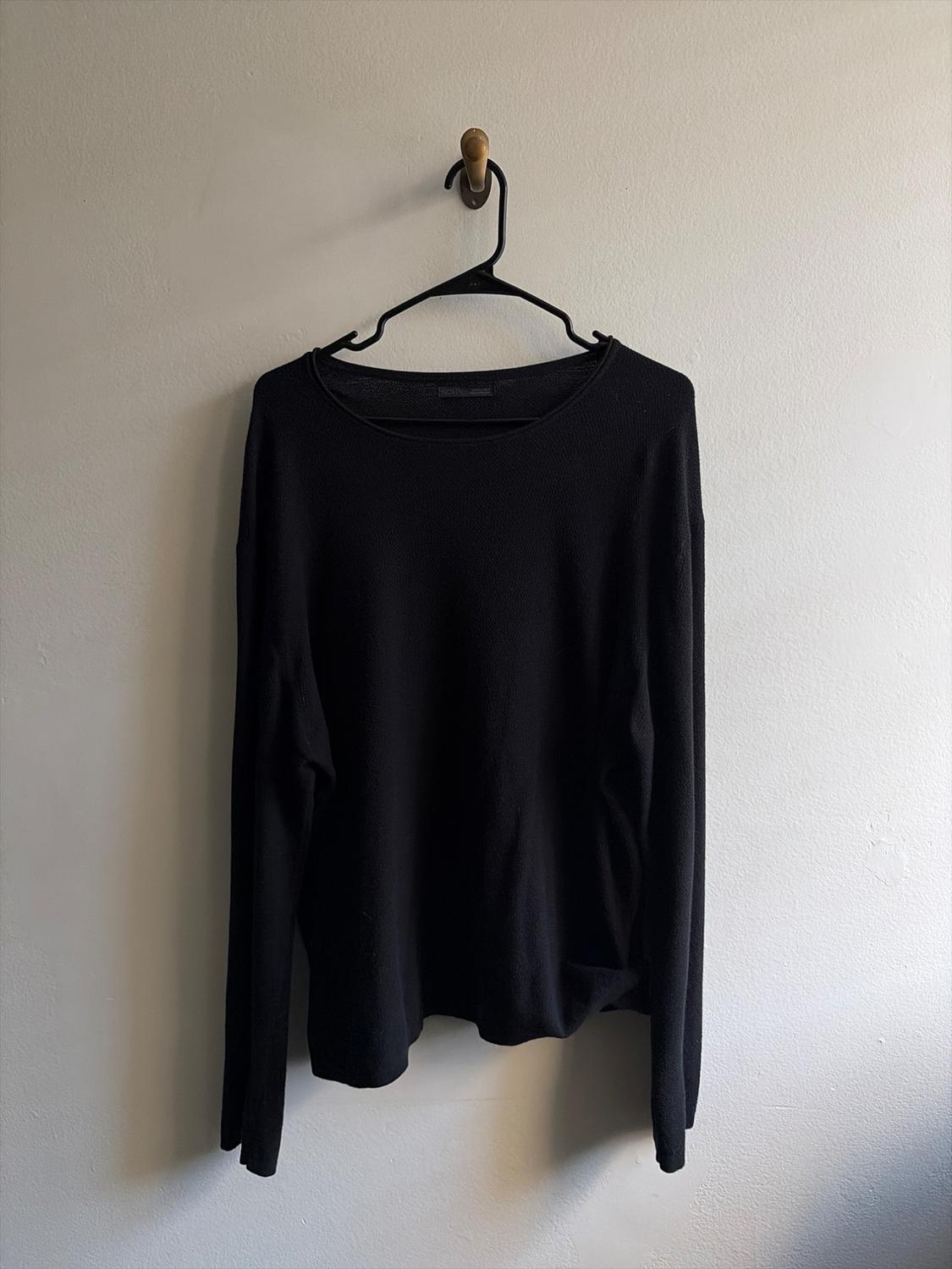 Black long-sleeve t-shirt with a crew neck, hanging from a hook on a white wall.