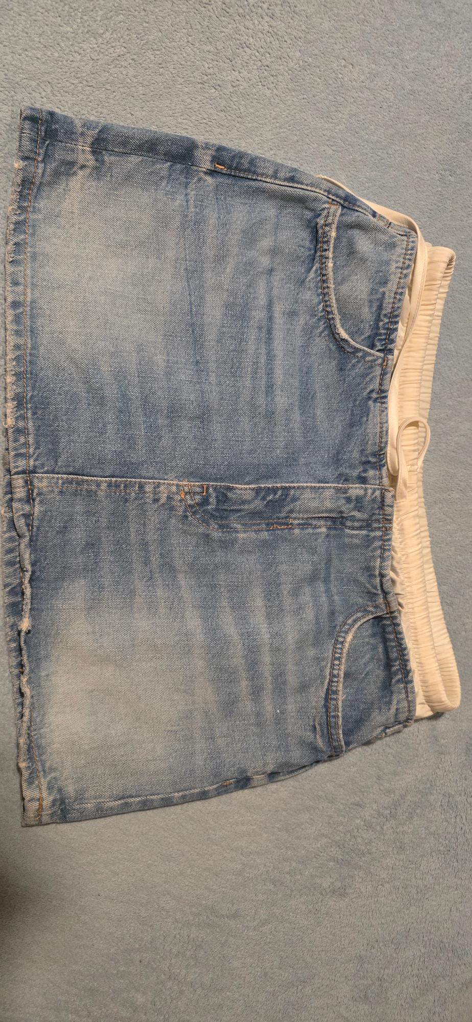 Light blue denim skirt with a white elasticated waist, on a grey surface. Casual, distressed design.
