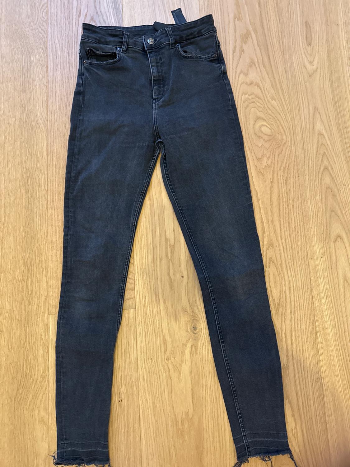 Dark, high-waisted denim jeans with a frayed hem, placed on a light wooden floor.