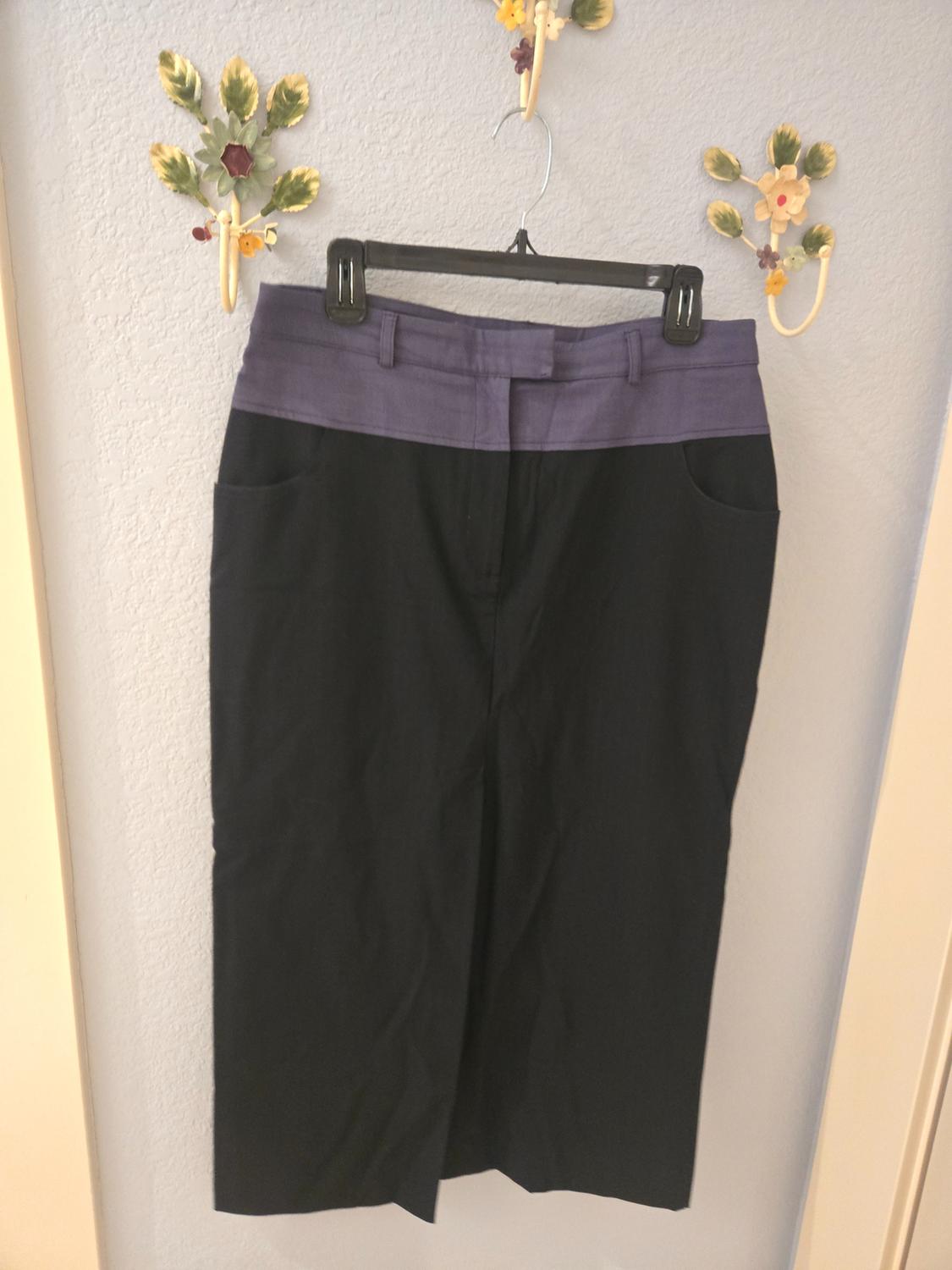 Black skirt with a purple waistband hanging on a black hanger against a white wall decorated with ceramic flowers.