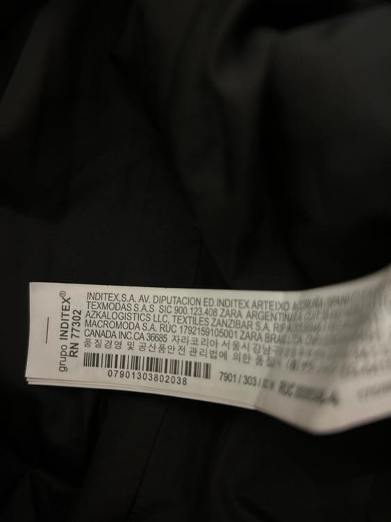 White clothing label with multi-language text, including "INDITEX S.A." and a barcode, on wrinkled black fabric.