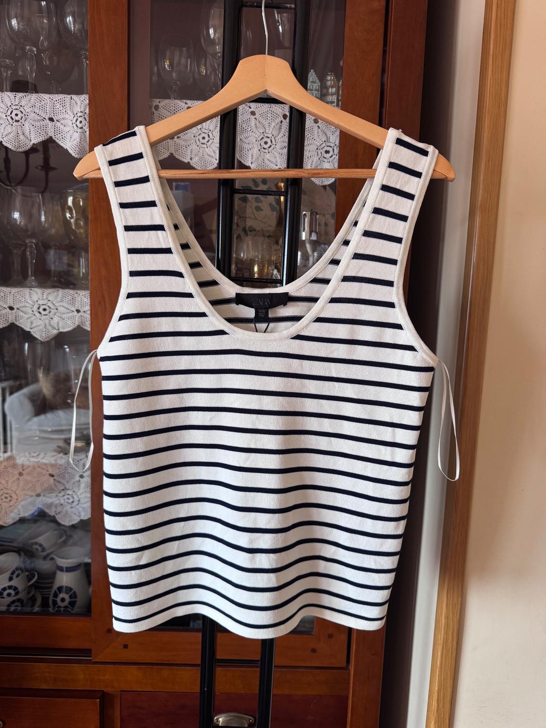 Black and white striped vest top hanging on a wooden hanger in front of a glass wardrobe with lace.