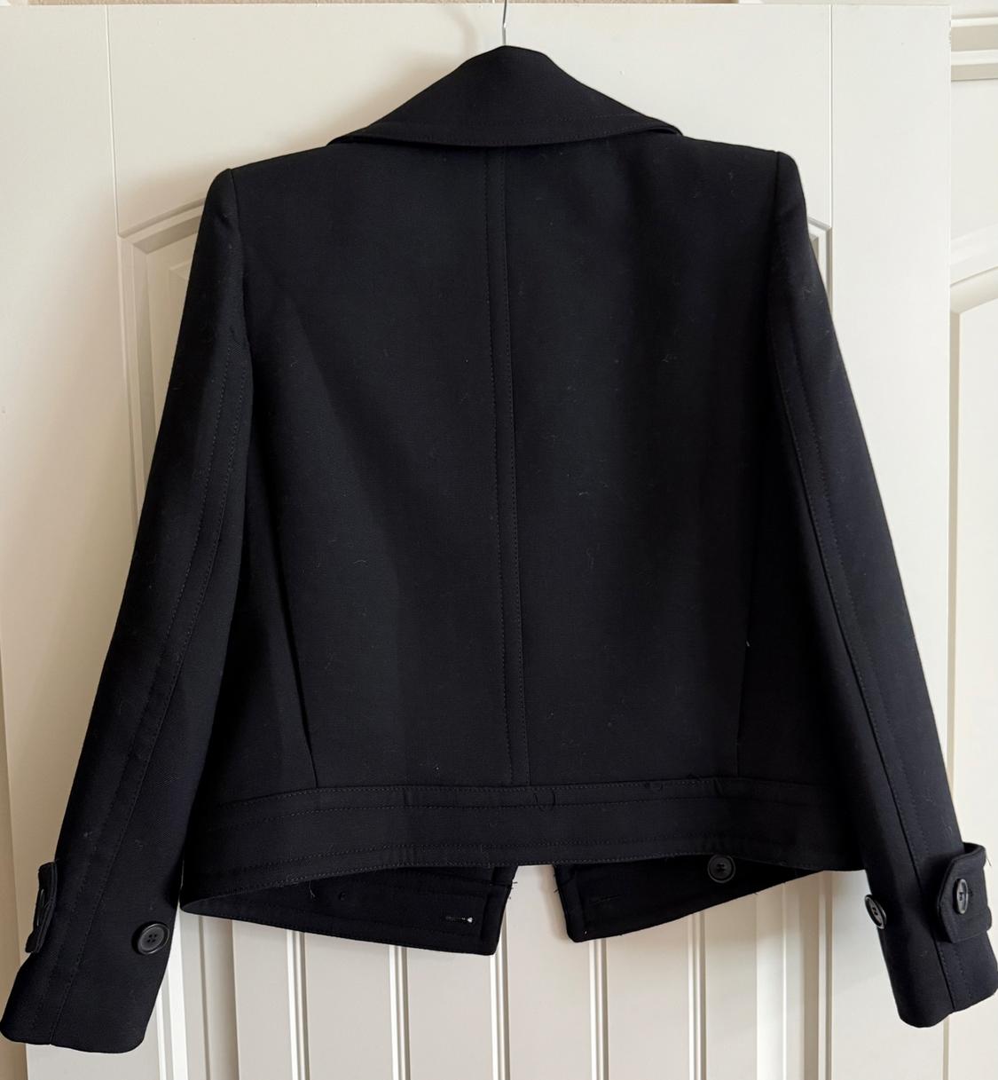 Back view of a black jacket with lapels and buttons on the cuffs.