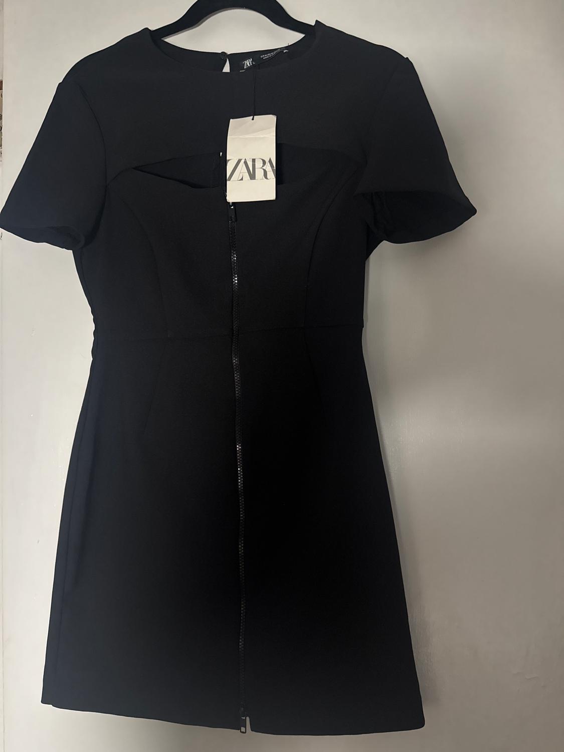 Short-sleeved black dress hanging on a hanger with a visible "ZARA" tag. Plain white background.
