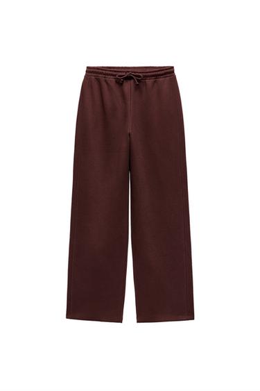 Front view of brown trousers with elasticated waistband and adjustable drawstring.