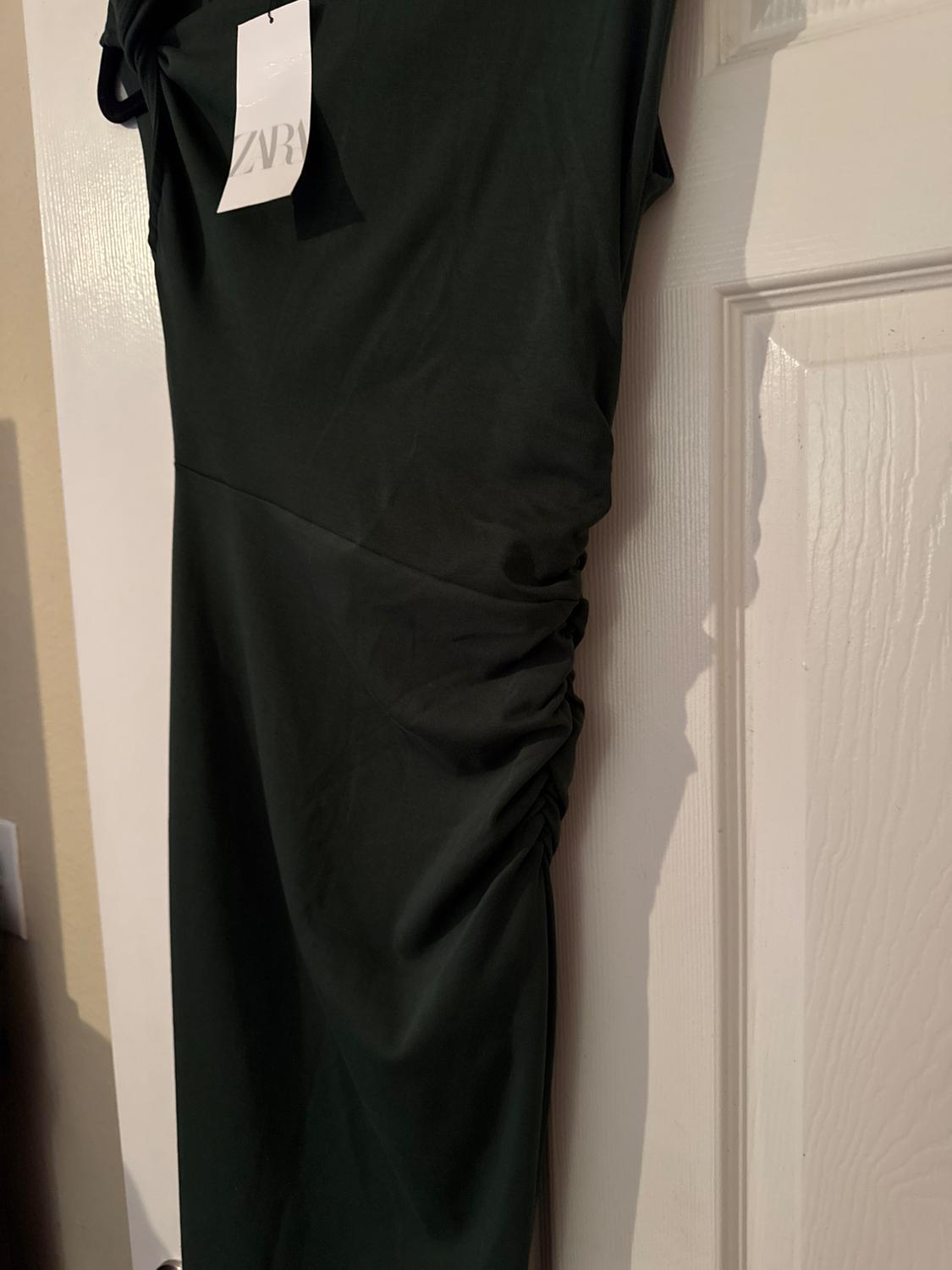 Black dress with side ruching hanging on a white door. Visible tag with the text "ZVRA".