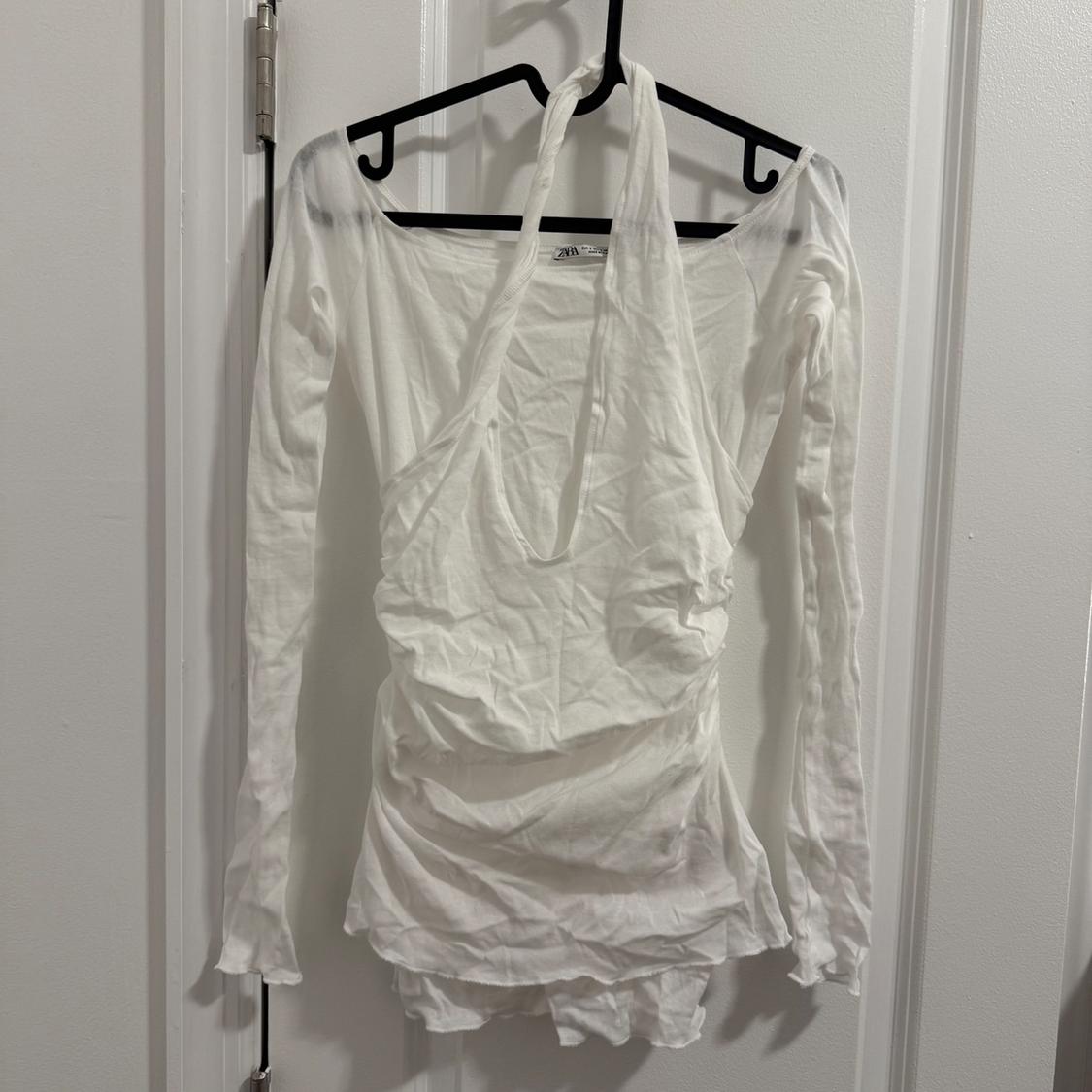 White long-sleeved halter-neck blouse, hanging on a black hanger over a white door.