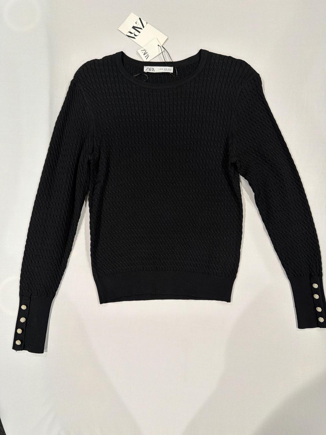 Textured knit jumper in black with a round neckline and decorative buttons on the cuffs against a white background. ZARA labels.